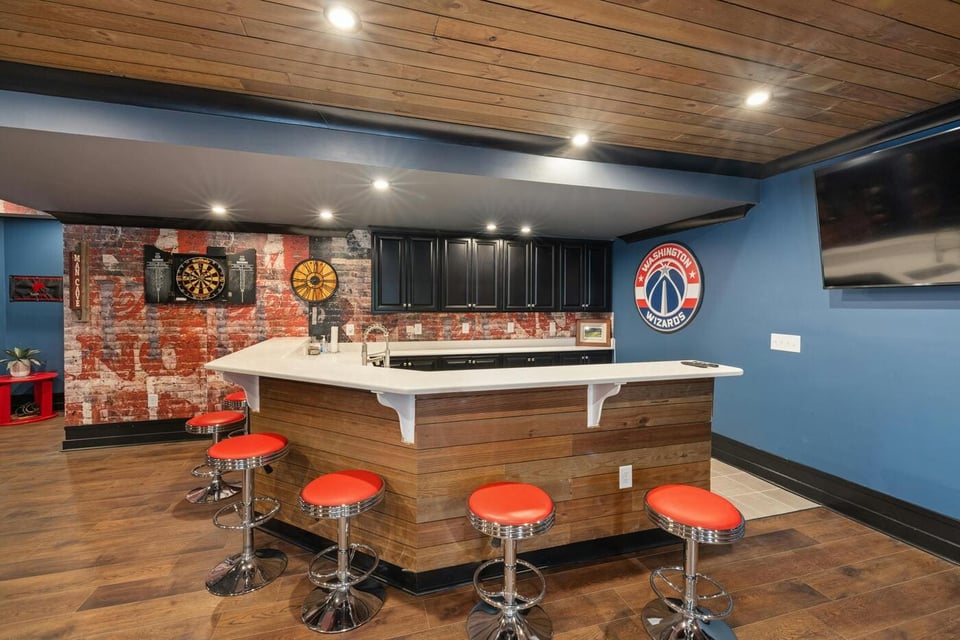 Stock image of basement bar with wood island, red stools, dartboard, and accent wall in East Hampton, CT