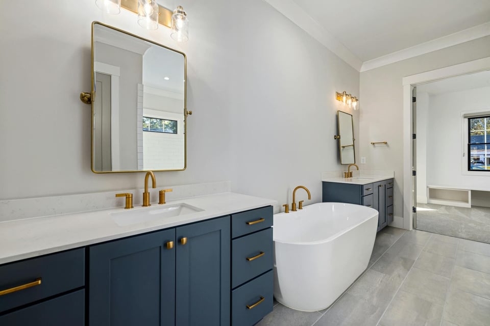 Stock image of bathroom with navy vanities, gold fixtures, freestanding tub, and double sinks in Colchester, CT