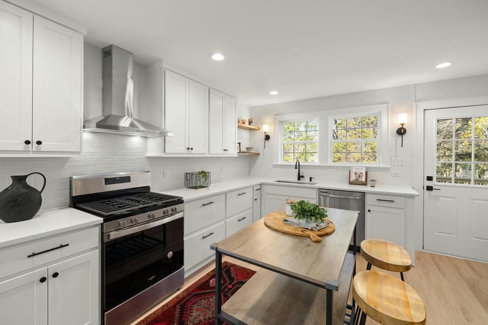 Stock image of bright kitchen with white cabinets, island table, gas range, and stainless appliances in Tolland, CT